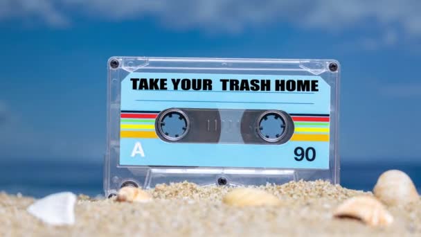 A cassette tape on a beach with words take your trash home - Footage, Video
