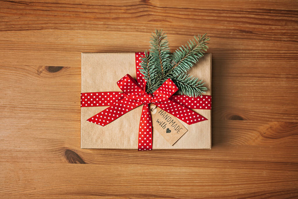 No hay ideas de regalo de Navidad para la familia, amigos para una Navidad anti-consumista. Caja de papel kraft regalo de Navidad con cinta roja, abeto y hecha a mano con etiqueta de amor en la mesa de madera. - Foto, Imagen