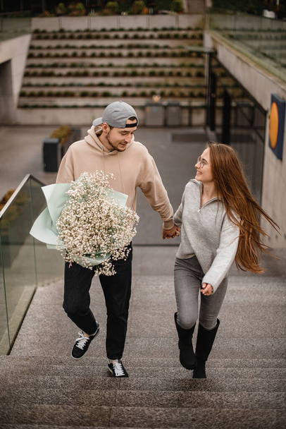 handsome young happy woman with long hair and man with bouquet of white flowers walks at street and looking at each other. Love story - Fotoğraf, Görsel