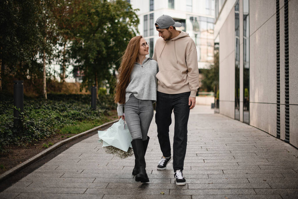 young happy couple in love of woman with long hair and bouquet of white flowers in her hand and man walks at street and looking at each other. Love story - Foto, Bild