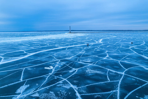 légi felvétel egy magányos világítótoronyról a fagyos tengeren. Fagyott kék jég repedések, drónra néző - Fotó, kép