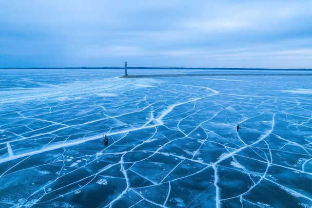 vista aérea de un faro solitario en el mar congelado. Hielo azul congelado en grietas, vista del dron - Foto, Imagen