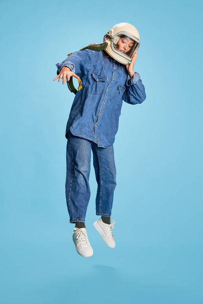 Portrait of young beautiful girl posing in astronaut helmet and special unifrom isolated over blue background. Concept of youth, beauty, fashion, lifestyle, emotions, facial expression. Ad - Φωτογραφία, εικόνα