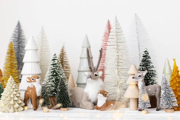 Stylish little Christmas trees and reindeer toys on white background. Festive Christmas scene, miniature snowy forest with cute deers. Merry Christmas! Modern decorations, holiday banner - Photo, Image