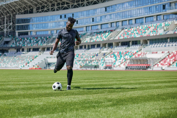 African American man playing football on the stadium field. A man runs with a soccer ball across the field. - Fotoğraf, Görsel