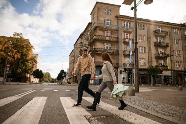 view on young beautiful couple in love holding hands and cross the road and look at each other - Valokuva, kuva