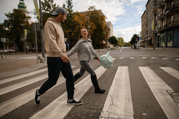 Young beautiful couple in love holding hands and cross the road and look at each other - Fotografie, Obrázek