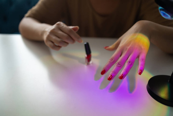 Woman paints her nails with red polish herself at home. Manicured red nails - 写真・画像