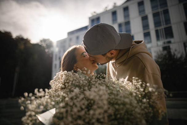 great close-up view on the heads of kissing young beautiful woman and man. Blurred floral bouquet in the foreground - Photo, Image