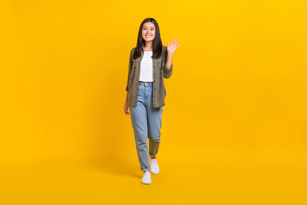 Ganzkörpergröße Foto von jungen niedlichen lächelnden Modell japanische Mädchen tragen lässiges Outfit Handfläche Schütteln hallo isoliert auf leuchtend gelben Farbhintergrund. - Foto, Bild