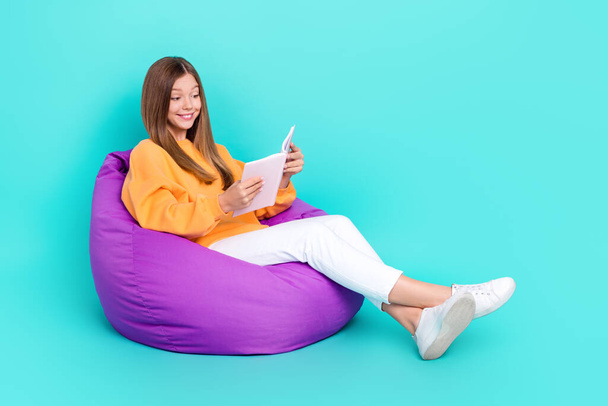 Full length photo of dreamy shiny school girl dressed orange hoodie bean bag interesting story empty space isolated teal color background. - Φωτογραφία, εικόνα