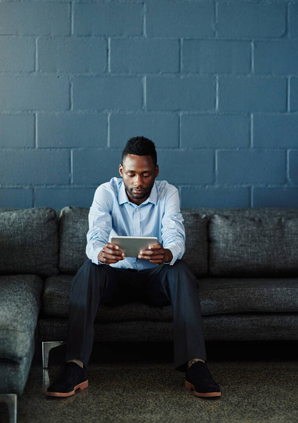 Comfort and connectivity. Full length shot of a handsome young businessman using his tablet while sitting on a sofa in the office - Fotó, kép