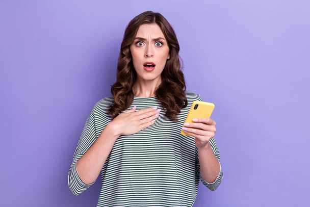 Photo of young scared terrified businesswoman hold smartphone unexpected message from customer bad comment isolated on violet color background. - 写真・画像
