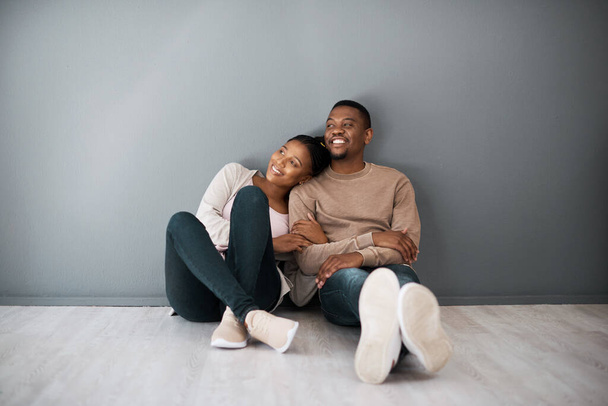 Apartment, love and couple on floor with wall background relax, rest and bond after moving in new home together. Real estate, dating and young black couple in living room thinking of house design. - Photo, Image