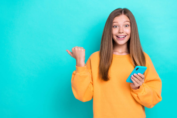 Photo of young excited positive cheerful girl addicted user hold her phone recommend mockup new ebay offer isolated on cyan color background. - Photo, Image