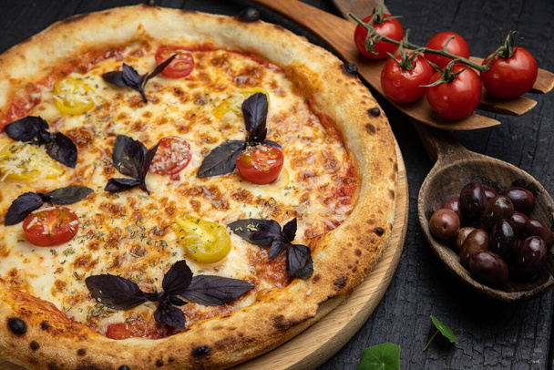 tasty pizza with cheese and vegetables on a wooden dark table - Zdjęcie, obraz