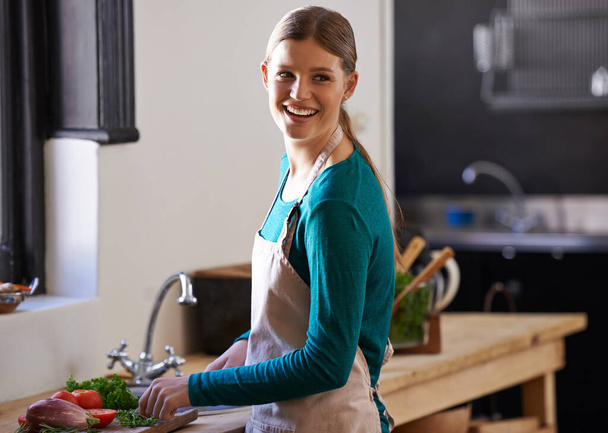 Veggies full of flavor. Portrait of an attractive young woman chopping vegetables in the kitchen - Photo, image
