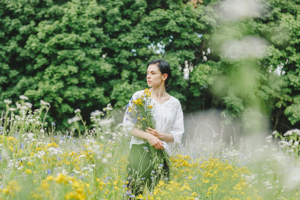 Девочка среди летнего поля крупным планом с полевыми цветами - Фото, изображение