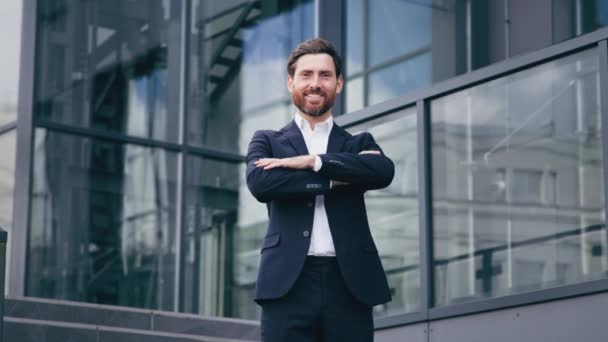 Successful confident businessman professional manager leader standing with arms crossed near corporate office building handsome smiling bearded caucasian man model posing outdoors in business center - Footage, Video