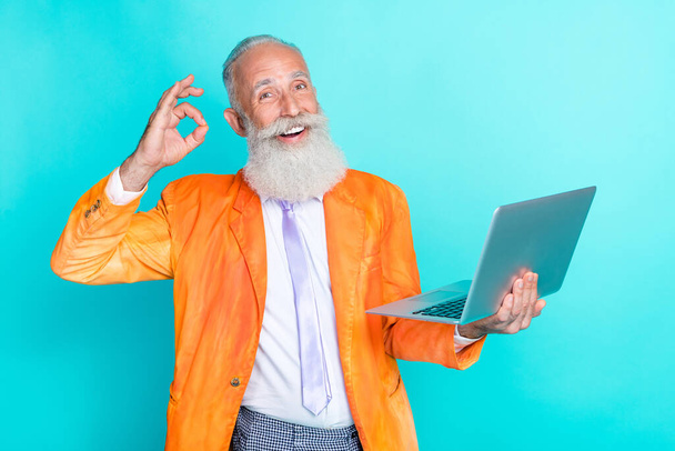 Photo of cheerful aged man hold netbook demonstrate okey symbol isolated on turquoise color background. - Fotoğraf, Görsel