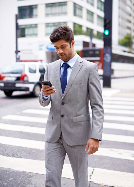 Getting around the city is easy with this navigation app. A cropped shot of a handsome young businessman texting while walking in the city - Photo, Image
