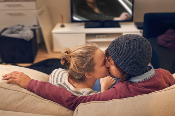 Μοιραζόμασταν ένα φιλί. ένα στοργικό νεαρό ζευγάρι που κλέβει ένα φιλί ενώ βλέπει τηλεόραση - Φωτογραφία, εικόνα