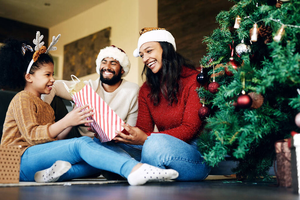 Family, christmas celebration and gift giving, happy smile and love on floor in home, festive holiday and surprise, Girl, mother and father celebrate xmas with present, happiness and bag in house. - Фото, изображение
