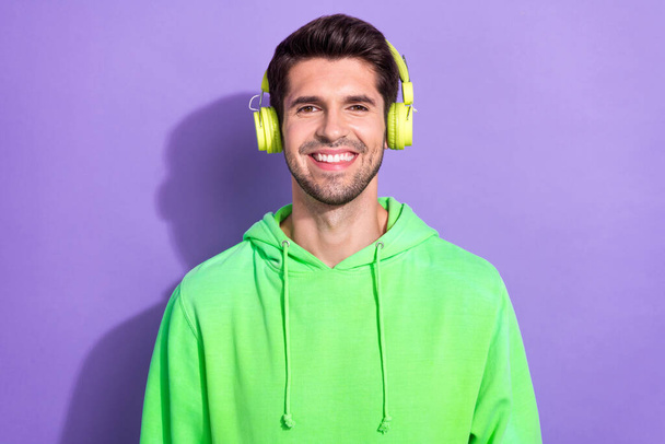 Photo of attractive positive guy brunet hairdo dressed green hoodie headphones listen favorite music isolated on purple color background. - Foto, Imagem