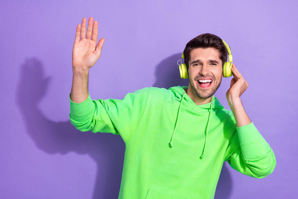 Portrait of optimistic handsome attractive guy brunet hairdo green hoodie touch headphones high five isolated on violet color background. - Foto, Imagen