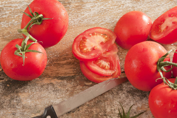 Świeże dojrzałe czerwone pomidory kratownicowe pokrojone ząbkowanym nożem kuchennym na autentycznej desce do rąbania drewna. - Zdjęcie, obraz