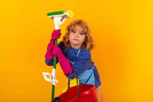 Dziecko sprząta w domu. Dzieciak sprzątanie mopem, aby pomóc w pracach domowych. Little cute boy zamiatanie i czyszczenie, izolowane na tle koloru studio - Zdjęcie, obraz