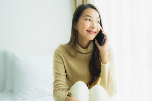 Nuori aasialainen nainen käyttää mobiili älypuhelin sängyssä makuuhuoneessa sisustus - Valokuva, kuva