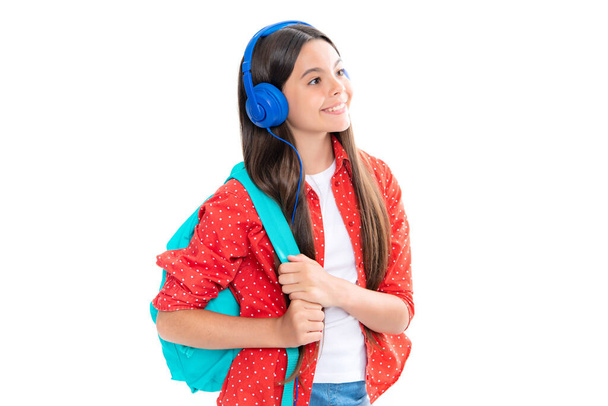 Κορίτσι του σχολείου, έφηβος φοιτητής με ακουστικά σε λευκό απομονωμένο φόντο στούντιο. Σχολική και μουσική εκπαίδευση έννοια. Πίσω στο σχολείο. Πορτρέτο του χαρούμενος χαμογελαστό έφηβο κορίτσι παιδί - Φωτογραφία, εικόνα