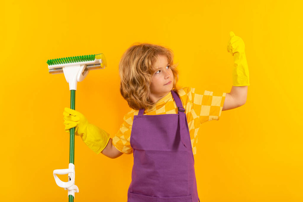 Kind reinigt thuis concept. Kind schoonmaken met dweil om te helpen met huishoudelijk werk. Kleine schattige jongen vegen en schoonmaken, geïsoleerd op studio kleur achtergrond - Foto, afbeelding
