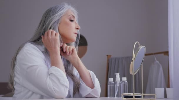 Starý 60s středního věku senior mature Kavkazská žena babička 50s dáma žena při pohledu na zrcadlo odraz dotýkat šedé vlasy tvář vrásky těšit účes péče vrásčité obličeje hydratační stárnutí - Záběry, video