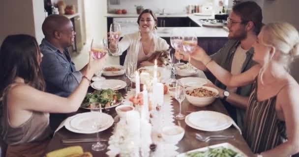 Barátok, éljenzés és vacsoraasztal együtt étkezésre, ételre vagy barátságra az ebédlőben otthon. Boldog emberek ünnepelnek, isznak és koccintanak a finom étkezésre, szocializálódnak vagy összegyűlnek nyaralni. - Felvétel, videó