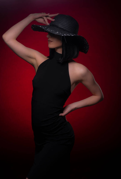 Seductive and attractive girl is posing on set while touching her hat and hiding her face with it - Photo, Image
