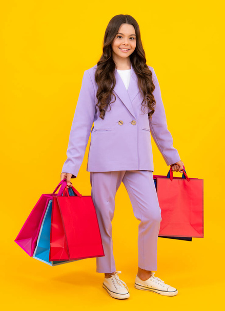 Funny teen girl hold shopping bag enjoying sale isolated on yellow. Portrait of teenager schoolgirl is ready to go shopping - Fotografie, Obrázek