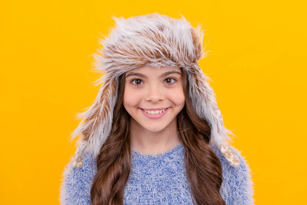 счастливая девочка-подросток в наушниках на желтом фоне, зимняя одежда. - Фото, изображение
