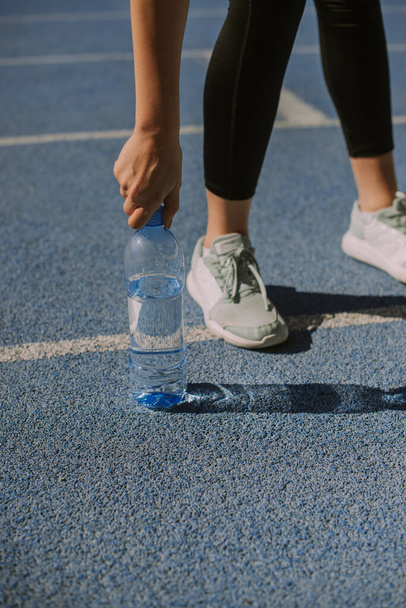 A female jogger is leaving the bottle of water on the sports track, after she is done with drinking - Photo, Image