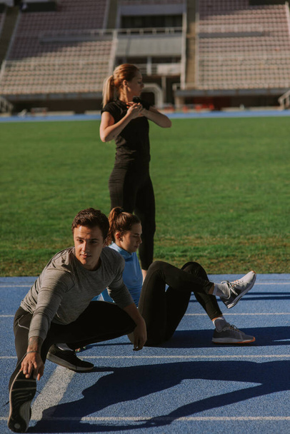 Young sportspeople are exercising together at the stadium, on a sunny morning - 写真・画像