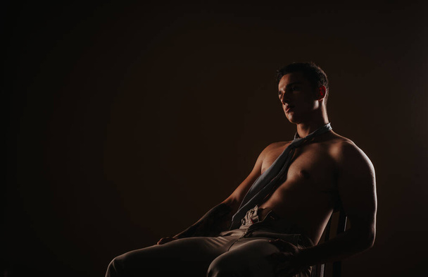 Hermoso modelo masculino mirando hacia otro lado mientras está sentado en el estudio - Foto, Imagen
