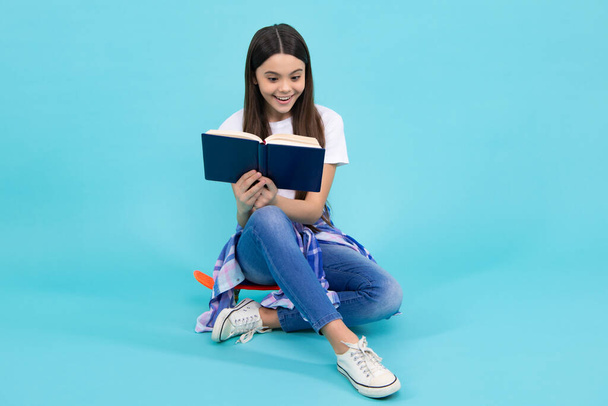 Повернутися до школи. Підліток школярка з книгою готова вчитися. Шкільна дівчинка діти на ізольованому синьому студійному фоні. Щасливий підліток, позитивні і усміхнені емоції дівчини-підлітка
 - Фото, зображення