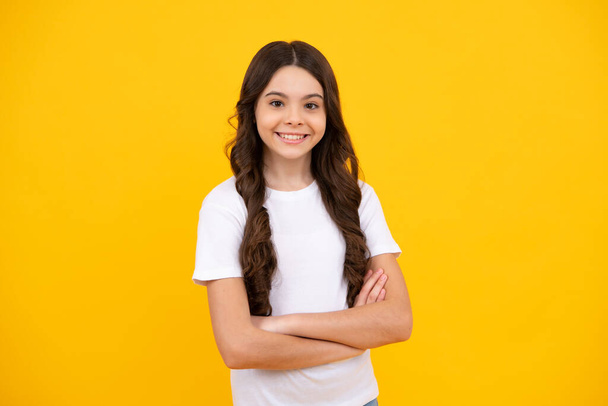 Happy teenager, positive and smiling emotions of teen girl. Cute little teenager girl crossing arms over yellow background - Photo, Image