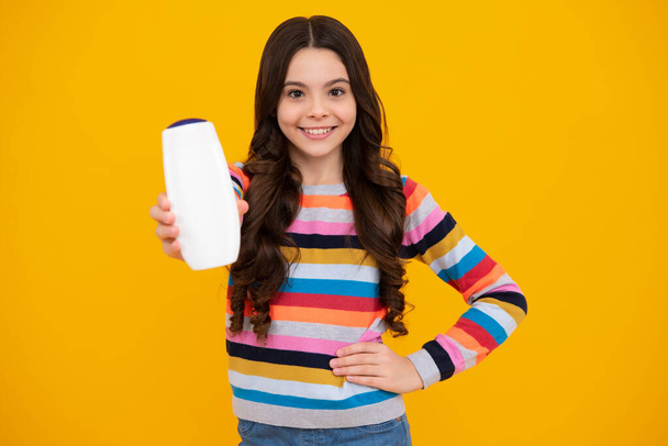 Menina adolescente mostrando condicionadores de xampu garrafa ou gel de chuveiro isolado no fundo amarelo. Produto cosmético de cabelo. Embrulha a garrafa. Adolescente feliz, emoções sorridentes de menina adolescente - Foto, Imagem