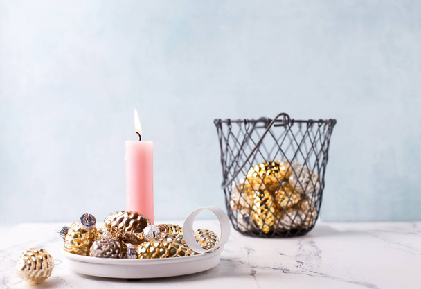 Winter holidays postcard. Pink burning candle and golden and silver decorative cones  against blue  textured wall. Selective focus. Place for text. - Foto, imagen