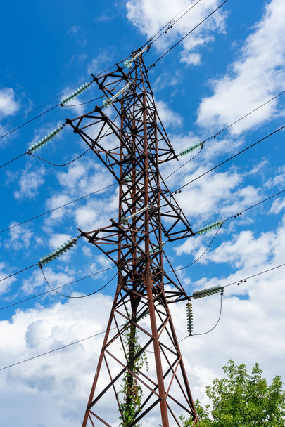Un poste de una línea eléctrica de alto voltaje en el fondo de un cielo azul con nubes blancas. - Foto, imagen