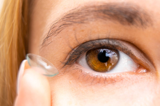 Mladá žena drží kontaktní čočky v blízkosti svého hnědého oka - Fotografie, Obrázek