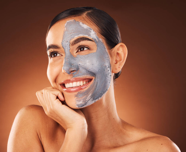 Πρόσωπο, ομορφιά περιποίηση δέρματος και γυναίκα με πήλινη μάσκα στο στούντιο απομονωμένη σε καφέ φόντο. Μακιγιάζ, αισθητική και χαρούμενη γυναίκα από τον Καναδά που σκέφτεται το υγιές και λαμπερό δέρμα μετά τη θεραπεία προσώπου. - Φωτογραφία, εικόνα