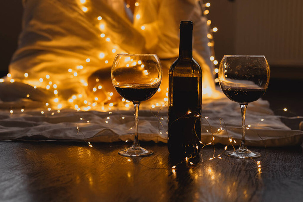 Романтический вечер дома бутылка вина и два бокала, гирлянда и праздничное настроение, День святого Валентина концепции празднования - Фото, изображение